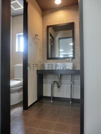 男女二つのトイレに挟まれた洗面台。照明の取り方や、床面のタイルがお洒落です